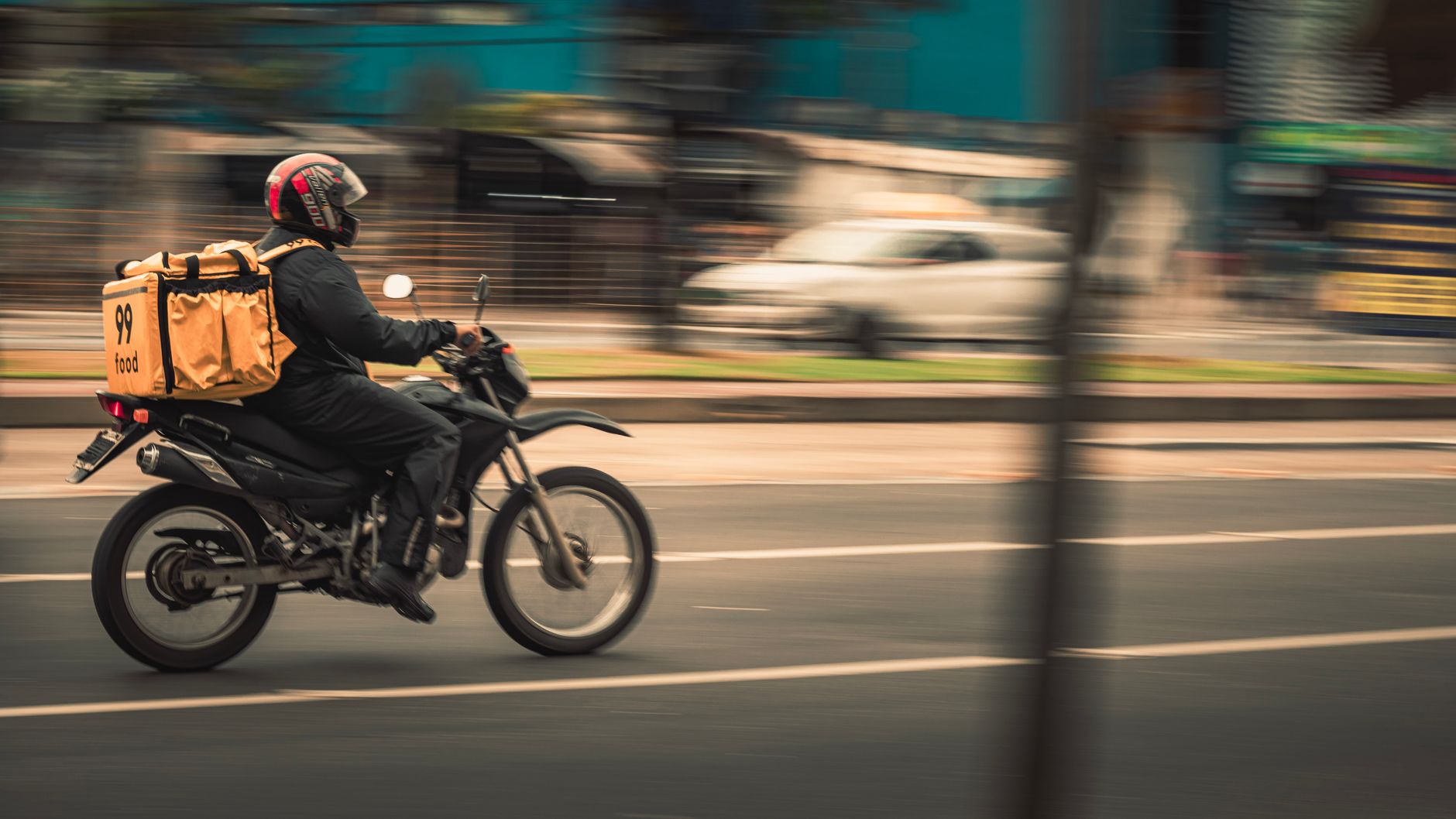 Entregador de moto com bag térmica em uma avenida